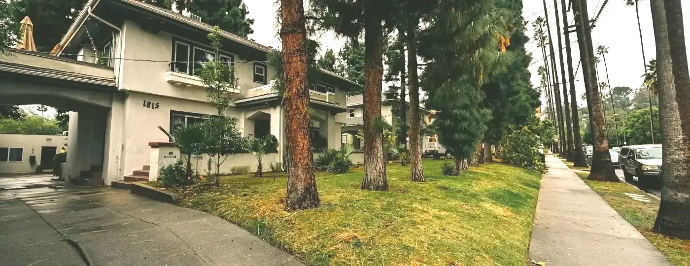 A row of low apartment buildings on a quiet Los Angeles street lined with tall trees