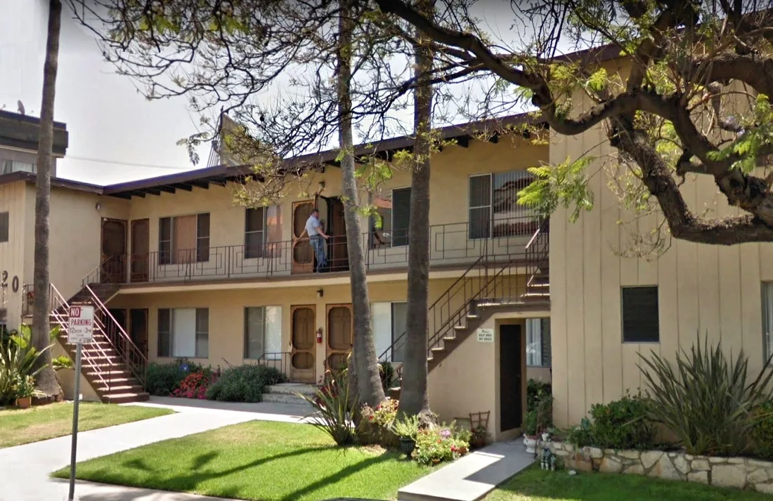 A two-story Los Angeles walk-up apartment building with exterior stairs, lawn and shade trees